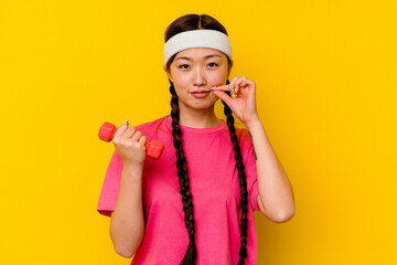 Young sport chinese woman isolated on yellow background with fingers on lips keeping a secret.