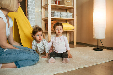 happy mom playing on the floor with two twin girls.