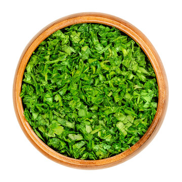 Chopped parsley, in a wooden bowl. Fresh, flat leaved parsley, green leaves of Petroselinum crispum, used as herb, spice and vegetable. Close-up, from above, isolated over white, macro food photo.