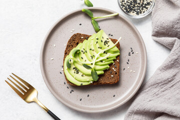 Whole grain rye bread toast with sliced avocado on white stone table background. Healthy avocado...