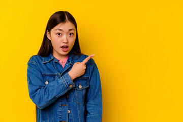 Young chinese woman isolated on yellow background pointing to the side