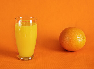 Fresh orange juice in glass and one whole orange  on a orange background.Monochromatic food photography.Copy space.