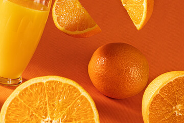 Fresh orange juice in glass and  falling  orange slices.Orange background.Monochromatic food...