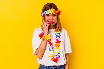 Young caucasian woman celebrating a hawaiian party isolated on yellow background biting fingernails, nervous and very anxious.