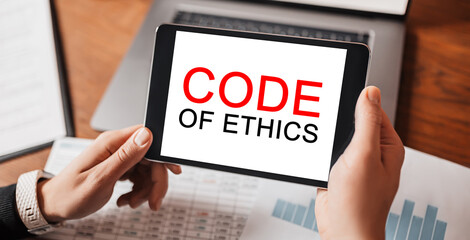 Man hands holding tablet with text Code of Ethics at workplace. Businessman working at desk with documents