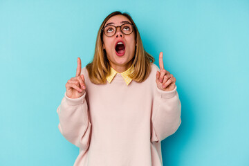 Young student caucasian woman isolated on blue background pointing upside with opened mouth.