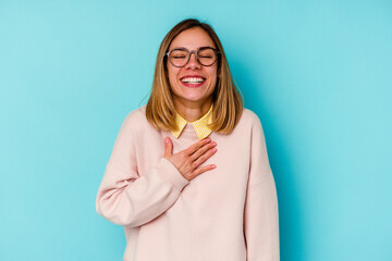 Young student caucasian woman isolated on blue background laughs out loudly keeping hand on chest.