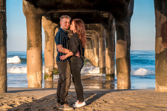 A man and a woman embrace under the pier at Manhattan Beach in Los Angeles in the early morning, a romantic trip