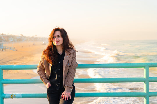 A young woman in a jacket stands on a pier overlooking the beach in the early morning, Los Angeles, California