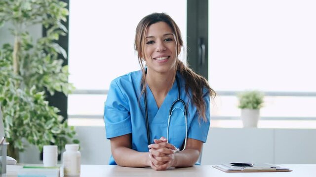 Video of attractive female doctor smiling looking at camera while working with laptop in the consultation.