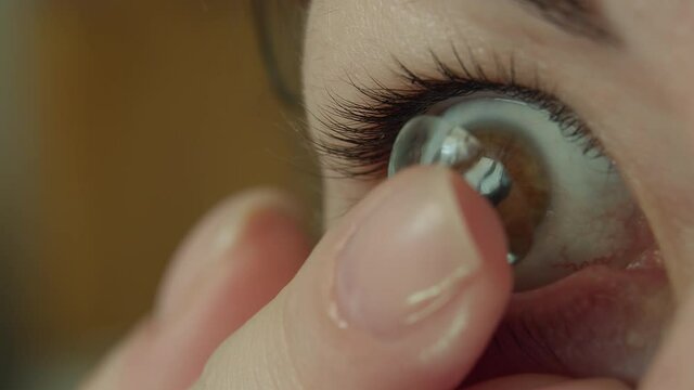 Woman with brown eyes putting on a soft contact lens on her eye, close-up