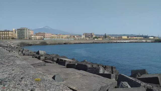Time lapse dal molo del porto di Catania in cui si vede la citt&agrave;, il vulcano Etna sullo sfondo e la stazione dei treni con un treno in movimento