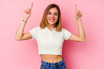 Young caucasian woman isolated on pink background indicates with both fore fingers up showing a...