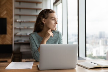 Pensive young female employee work on computer in office look in distance thinking pondering of...