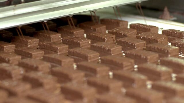 It is poured over the cakes with chocolate. Nougat and peanut chocolate production. The chocolate bars move along the conveyor belt in the confectionery factory for confectionery production. 