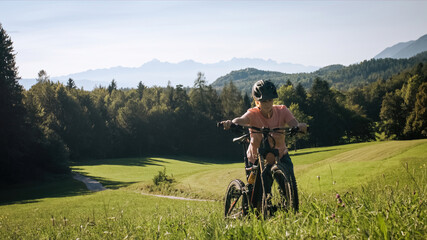 Obraz premium Woman walking uphill with mountain bike in nature on a beautiful day.