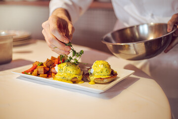 chef preparing eggs benedict in a kitchen at a fine dining restaurant during brunch