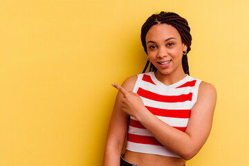 Young african american woman isolated on yellow background smiling and pointing aside, showing something at blank space.