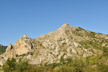 landscape with a small mountain and dense greenery at the base against a clear blue sky shot in...