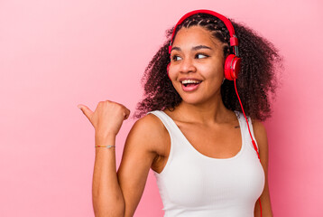 Obraz na płótnie Canvas Young african american woman listening to music with headphones isolated on pink background points with thumb finger away, laughing and carefree.