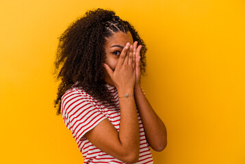 Young african american woman isolated on yellow background blink through fingers frightened and...