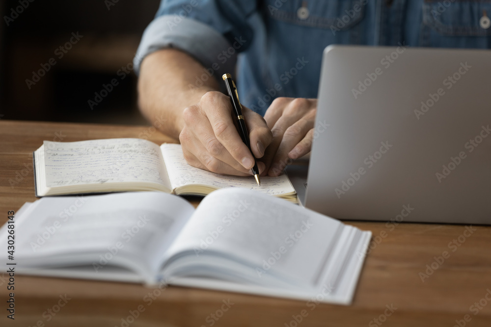 Wall mural crop close up of male student make notes handwrite in notebook study online on computer from home. m