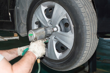 The car mechanic uses a pneumatic wrench to tighten the wheel nut