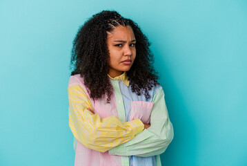 Young african american woman isolated on blue background frowning face in displeasure, keeps arms...
