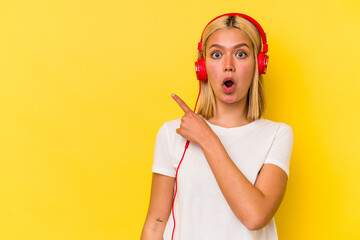 Young venezuelan woman listening music isolated on yellow background pointing to the side
