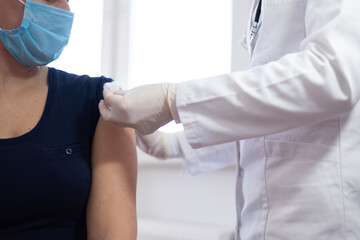 Female doctor holding syringe and using cotton before make injection to patient in medical mask. Covid-19 or coronavirus vaccine