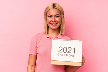 Young venezuelan woman holding a calendar isolated on pink background happy, smiling and cheerful.