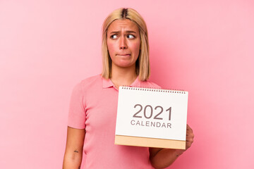 Young venezuelan woman holding a calendar isolated on pink background confused, feels doubtful and unsure.