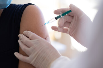 Coronavirus vaccination, doctor injecting a patient, getting first shot of covid vaccine in arm muscle. Medical doctor in protective suit and mask, process of immunization against covid-19