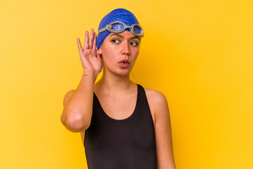 Young swimmer venezuelan woman isolated on yellow background trying to listening a gossip.