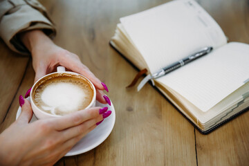 Female hands and coffee, office supplies with workspace on a wooden table, top view.