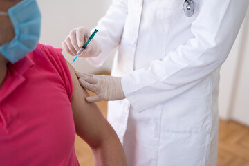 Coronavirus vaccination, doctor injecting a patient, getting first shot of covid vaccine in arm muscle. Medical doctor in protective suit and mask, process of immunization against covid-19