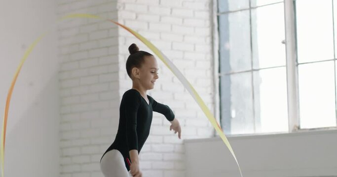 Teen girl wearing black leotard dancing. Young gymnast practicing moves and elements with a ribbon - childhood dream 4k footage