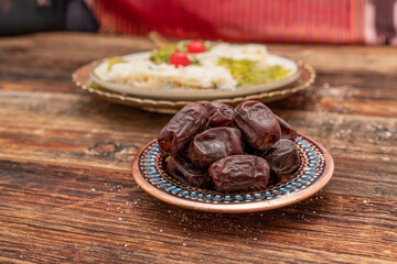 Fresh date fruits in ottoman handmade bowl on the front and Traditional Turkish milky Ramadan Dessert named Gullac on the background. White wooden background. Ramadan (Ramazan) food for iftar or sahur