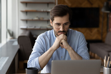 Pensive young businessman look at laptop screen think ponder of problem solution. Thoughtful male...