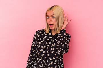 Young venezuelan woman isolated on pink background trying to listening a gossip.