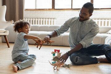 Happy dad and toddler son creating dinosaurs battle in prehistoric world, fighting with small toy...