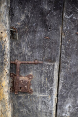 close up of an old and deteriorated wooden door with a rusty metal latch and a padlock, rural texture, vertical