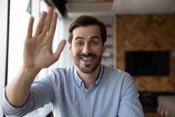 Headshot portrait of smiling young Caucasian man look at camera wave greet talk on video call online. Screen view of happy millennial male have webcam zoom digital conference. Virtual event concept.