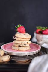 Chocolate chip cookies with organic strawberry in a pink plate on a black wooden background, close up, still life photography