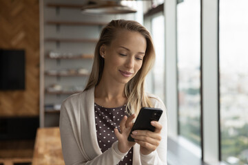 Young Caucasian businesswoman hold use modern cellphone text or message online on gadget. Millennial woman look at smartphone screen browse wireless internet on device. Communication concept.