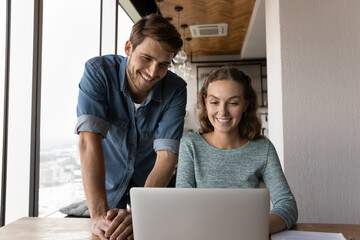 Happy diverse businesspeople gather in office look at laptop screen work on financial business project together. Smiling colleagues cooperate brainstorm over startup on computer. Teamwork concept.