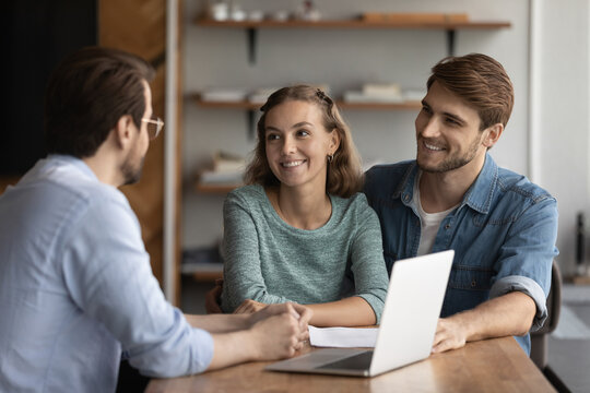Happy young Caucasian couple clients buyers talk speak with male real estate agent or broker about own house purchase. Smiling man and woman have consultation with relator at meeting in office.