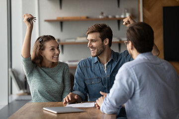 Excited young Caucasian man and woman clients hold keys to new home buy first shared house...
