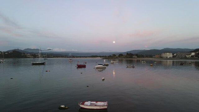 Barcos parados en el agua con una preciosa luna llena al fondo y con el cielo te&ntilde;ido de rosa al atardecer.
