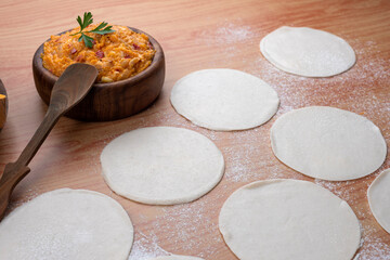 Empanadas tapas on wooden board and stuffed with vegetables and squash with bowl and flour preparation for Argentine empanadas
